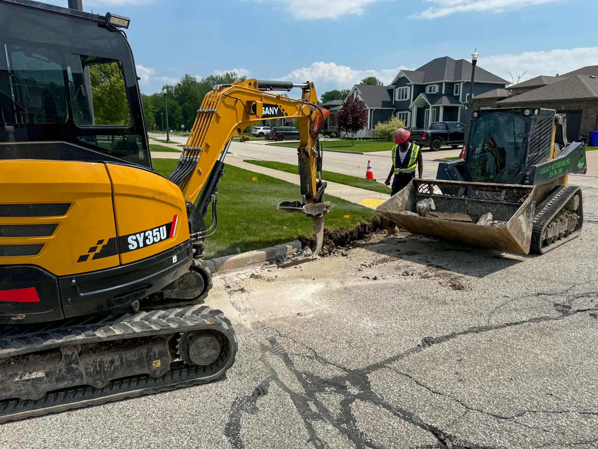 SANY excavator and skid steer trenching at the curb in a residential neighbourhood